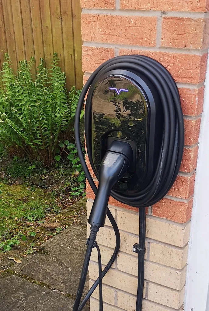 Black EV charger with coiled cable installed on a red brick wall